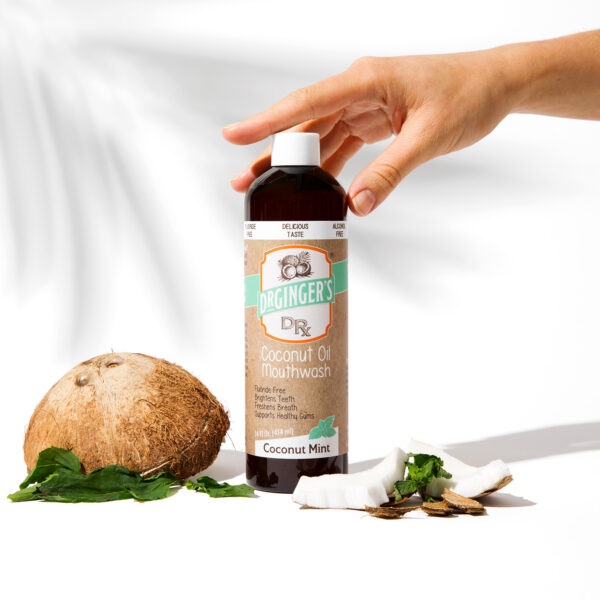 Dr. Ginger's Coconut Oil Mouthwash sitting next to mint leaves and a coconut