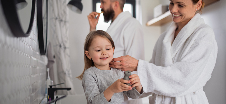 A father and mother with small daughter washing indoors in bathroom in the evening or morning.